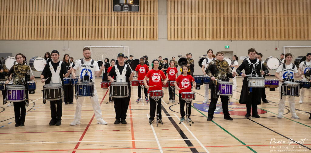 Large group of percussionists in a gym, standing with snare drums ready for a drumline performance.