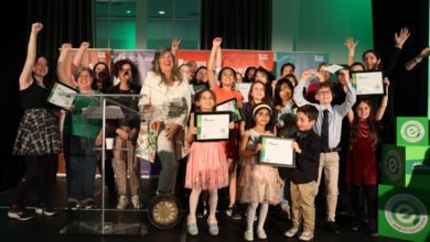 Group of children and adults on a stage, holding framed certificates and cheering during an awards ceremony.