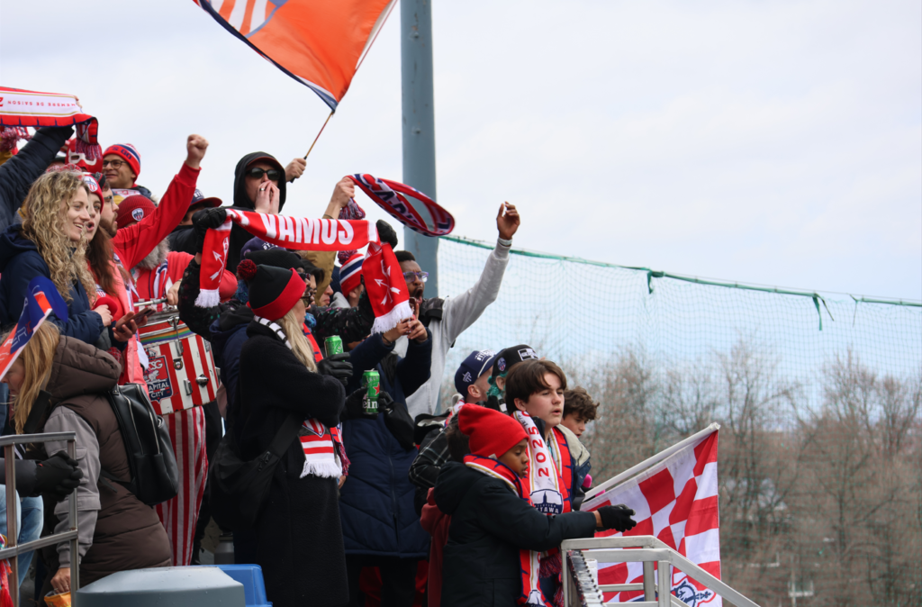 Crowd of football fans in red and white, cheering with scarves and flags in the stadium stands.
