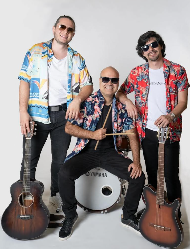 Three male musicians in colorful Hawaiian shirts pose with guitars; a drummer sits center with drumsticks in front of a Yamaha drum set, all wearing sunglasses.