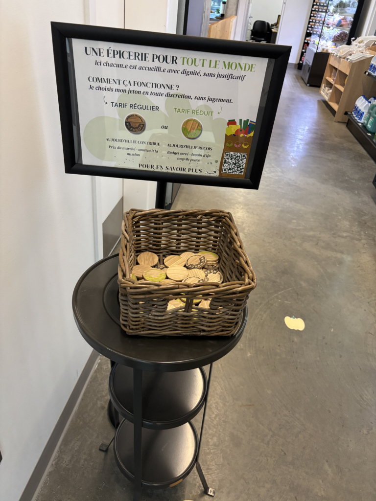 Framed information sign on a black stand with a wicker basket filled with round wooden tokens, in a store aisle setting.