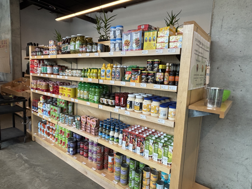 Wooden grocery shelf full of jars, bottles, and boxed foods in a warehouse showroom setting.