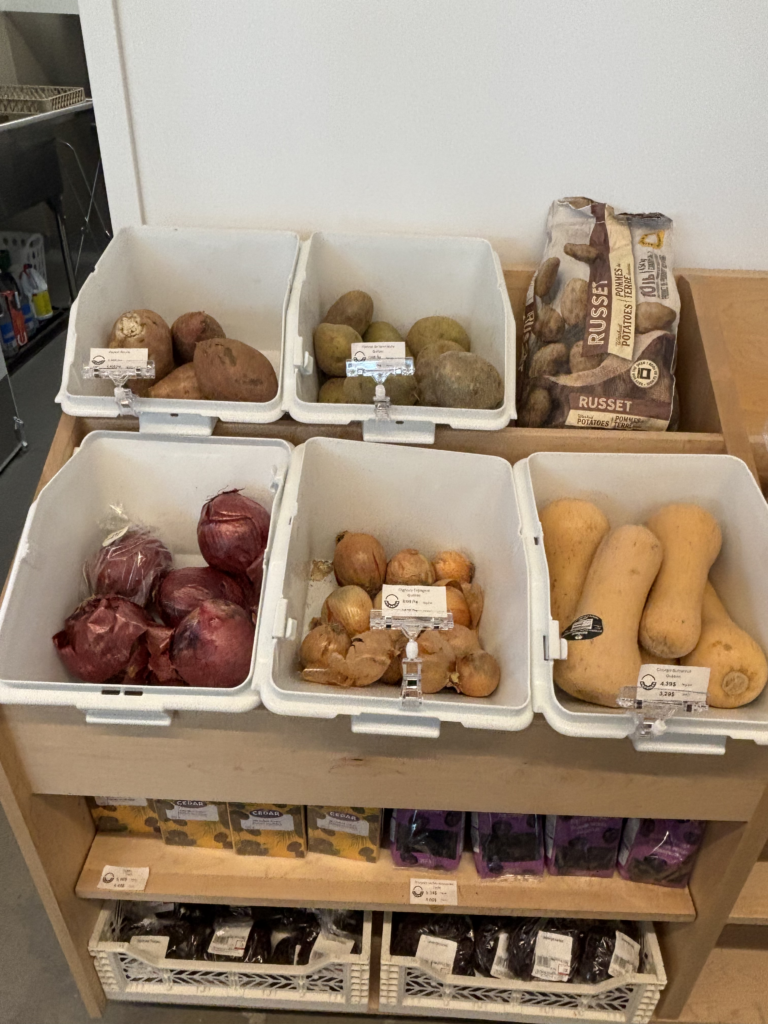 White bins display assorted root vegetables: potatoes and onions in a grocery store produce area.
