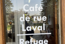 Glass door with white text reading 'Bienvenue Café de rue Laval Refuge', reflecting trees outside.