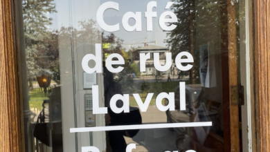 Glass door with white text reading 'Bienvenue Café de rue Laval Refuge', reflecting trees outside.