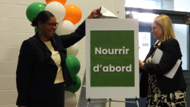 Two women in business attire attach a green-framed sign reading 'Nourrir d'abord' beside a balloon column.