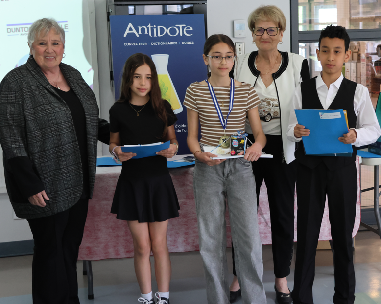 Five people posing at an award ceremony: two adults and three students holding awards, with an Antidote banner in the background.