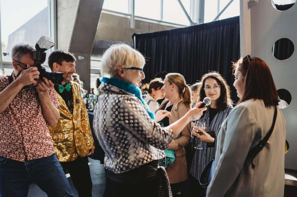 image Média Laval Photographer filming a social event as an interviewer speaks into a mic to a guest holding a glass.