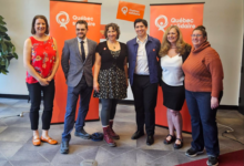 Six adults pose for a group photo indoors with orange Québec solidaire banners in the background.
