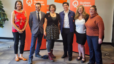 Six adults pose for a group photo indoors with orange Québec solidaire banners in the background.