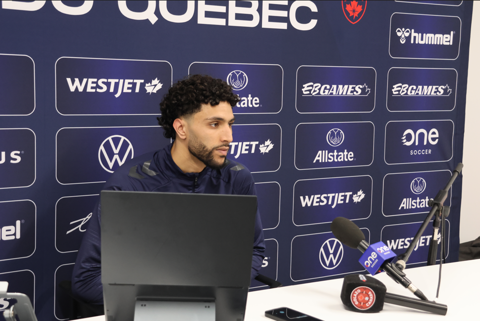 Athlete sits at a press conference table with a branded backdrop featuring WestJet, Allstate, and other logos behind him.