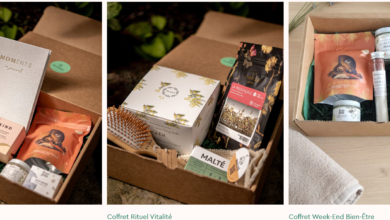 Open gift box with assorted natural skincare and wellness items, including a gray 'MOMENTS' box and pink BKIND packaging on a plant background.