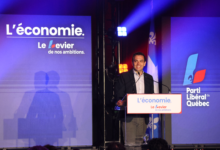 Man at a podium giving a speech on a blue campaign stage with 'L'économie' slogan and Parti Libéral du Québec banners