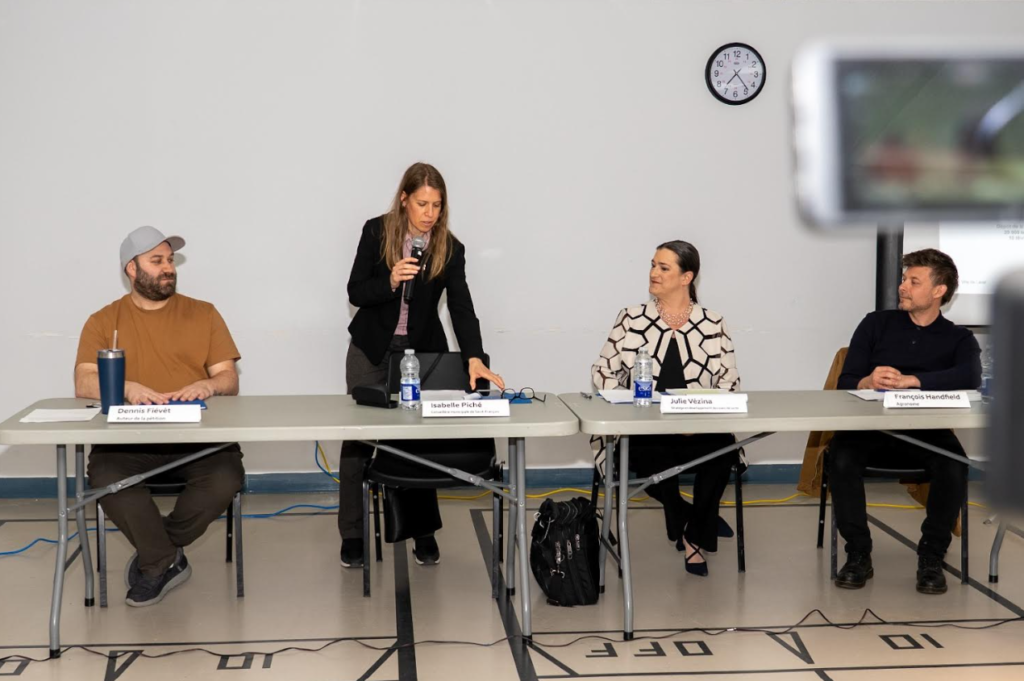 image Média Laval Panel discussion with four people seated at a long table; woman in the center speaks into a microphone while the others listen.