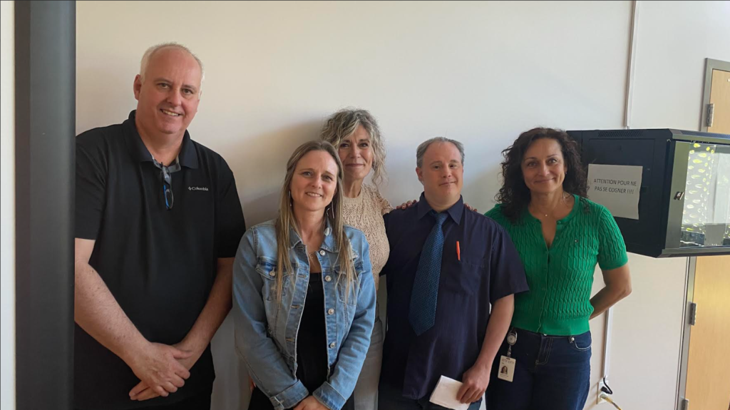Média Laval Five adults smiling and posing together in a bright office hallway.