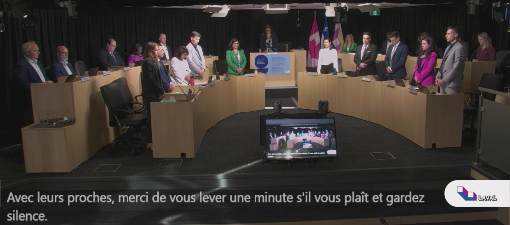 Conseil municipal juin 2026 Média Laval Municipal council meeting in progress with representatives standing around a U-shaped desk; Laval logo visible in the foreground.