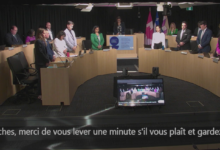 Municipal council meeting in progress with representatives standing around a U-shaped desk; Laval logo visible in the foreground.