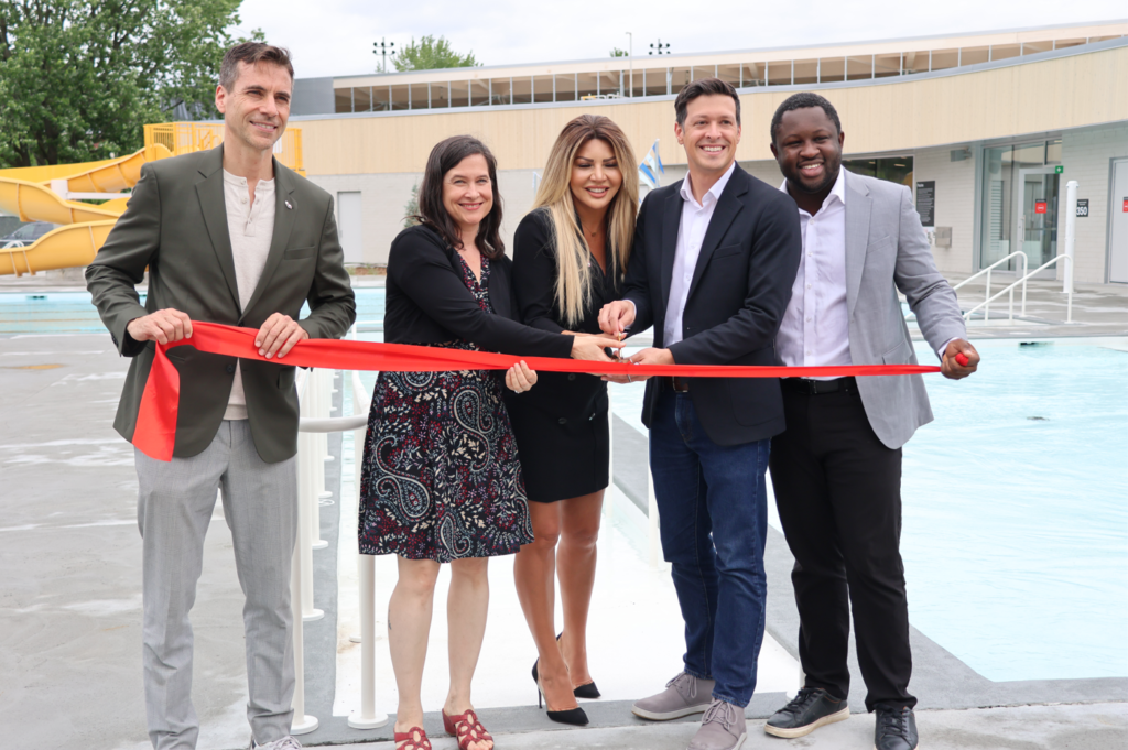 Five people cut a red ribbon at a poolside ribbon-cutting ceremony, smiling for the camera.