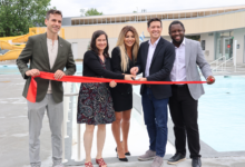 Five people cut a red ribbon at a poolside ribbon-cutting ceremony, smiling for the camera.