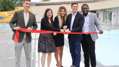 Five people cut a red ribbon at a poolside ribbon-cutting ceremony, smiling for the camera.