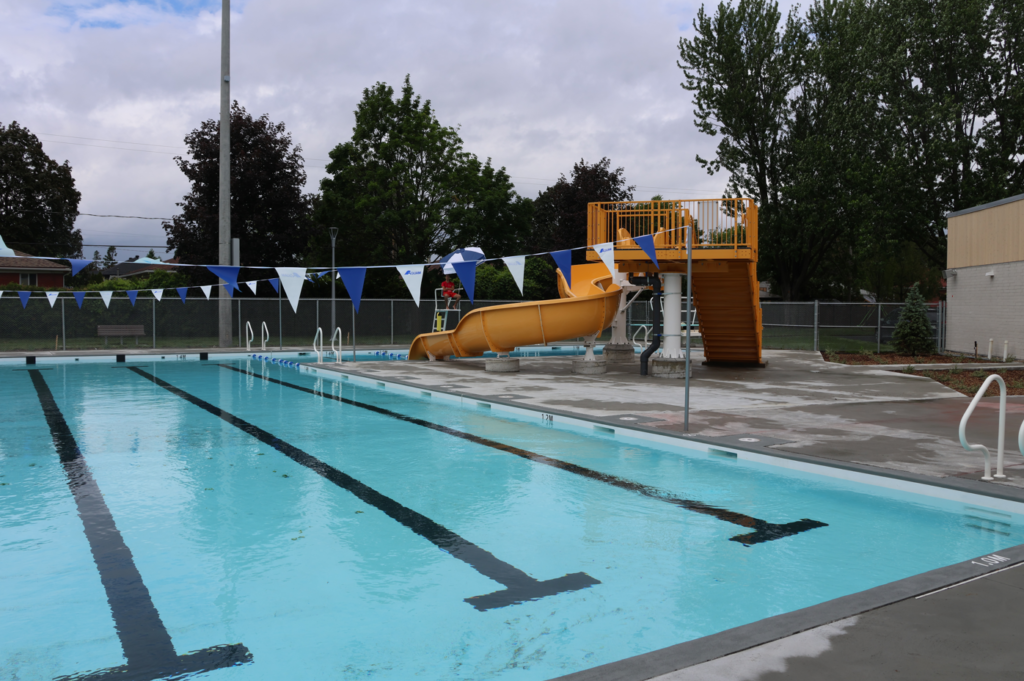Outdoor pool area with a bright yellow twisty slide and blue‑and‑white pennant bunting along the fenceIdeal for a public pool site or recreation area, not a close-up image
