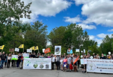 Group of diverse people holding environmental protest banners and signs outdoors on a sunny day with trees in the background.