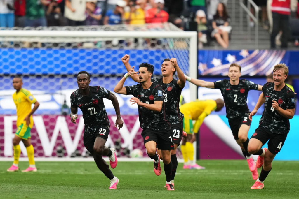 Soccer à Laval Média Laval Five soccer players in black uniforms celebrate a goal, sprinting past the goal with raised arms and fans in the background.