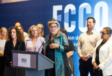 Group of professionals at a podium during a press conference, blue backdrop with FCCO logo behind them, central speaker gesturing.