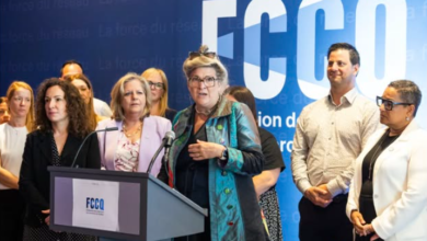 Group of professionals at a podium during a press conference, blue backdrop with FCCO logo behind them, central speaker gesturing.