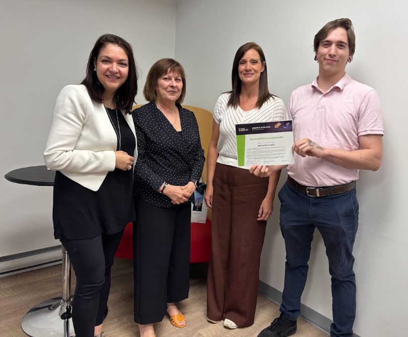 image Média Laval Four coworkers pose in an office; the woman in white holds a certificate.