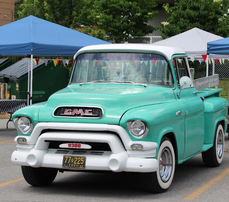 Vintage turquoise GMC pickup truck at a daytime outdoor car show; retro style with white roof and chrome bumper.
