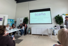 Group of people seated around a long table in a bright meeting room, watching a projector screen displaying a slide with a 'scania' logo and French text.