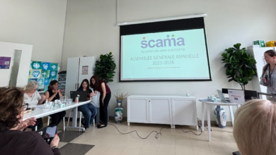 Group of people seated around a long table in a bright meeting room, watching a projector screen displaying a slide with a 'scania' logo and French text.