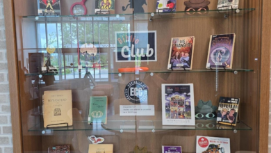 Glass-front book display case with shelves of colorful children's books and props, including magnifying glass and hat silhouettes, centered around a 'Club' sign.