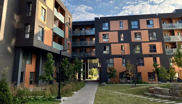 Modern apartment complex with orange and dark gray panels, a central walkway, and trees in a courtyard.
