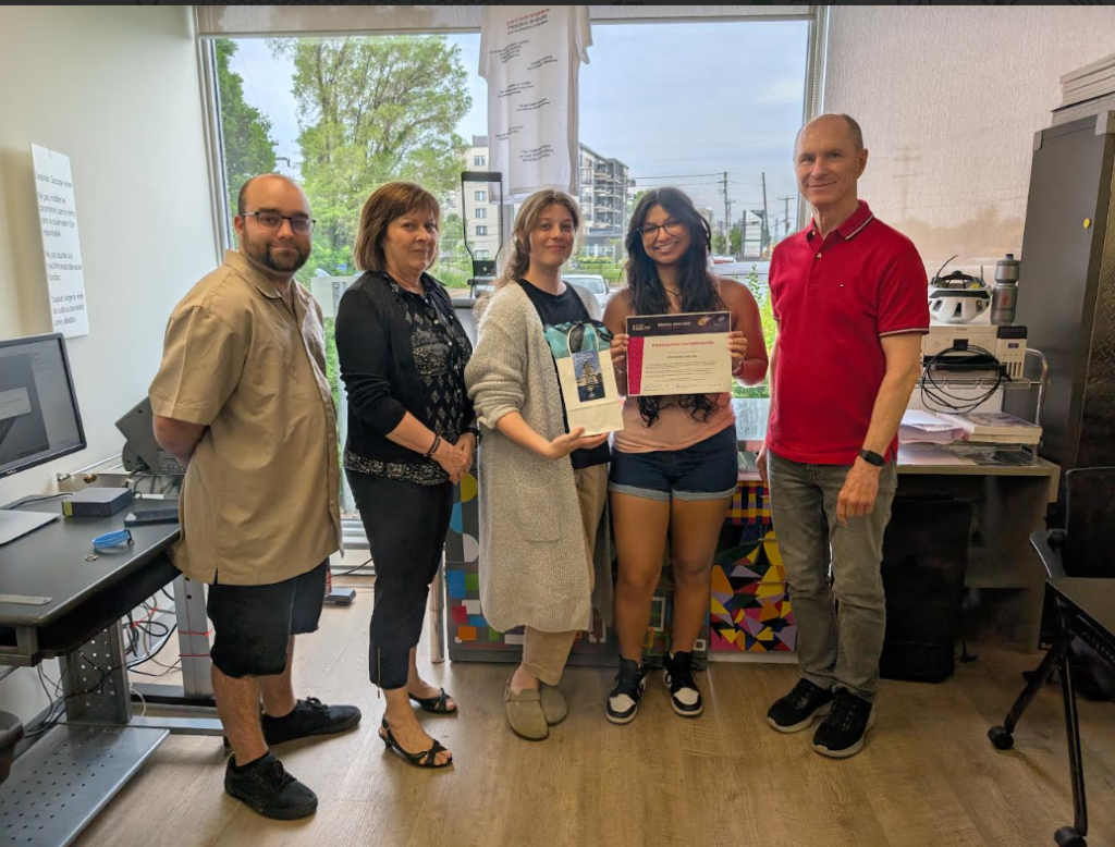 image Média Laval Six adults in an office pose for a photo; a young woman in pink holds a certificate while five colleagues stand beside her.