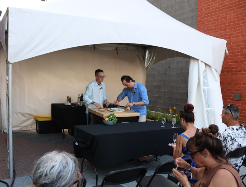 image Média Laval Two chefs demonstrate cooking at a wooden cutting board inside a white event tent as a small audience watches.
