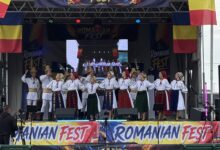 Stage performance at Romanian Fest with dancers in traditional folk costumes and Romanian flags on both sides of the banner.