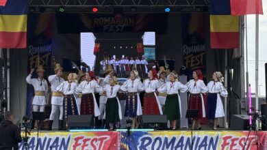 Stage performance at Romanian Fest with dancers in traditional folk costumes and Romanian flags on both sides of the banner.