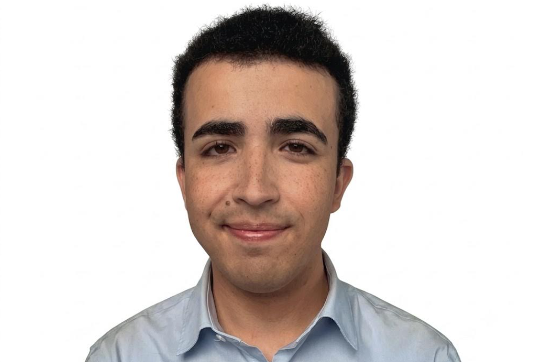Portrait of a young man with short black hair in a light blue shirt, facing the camera against a white background.